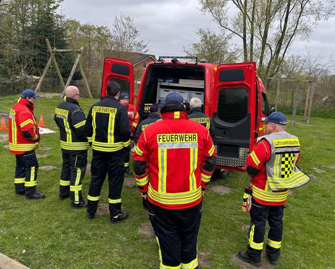 Mehrere Feuerwehrleute stehen vor den geöffneten Türen eines Feuerwehrwagens